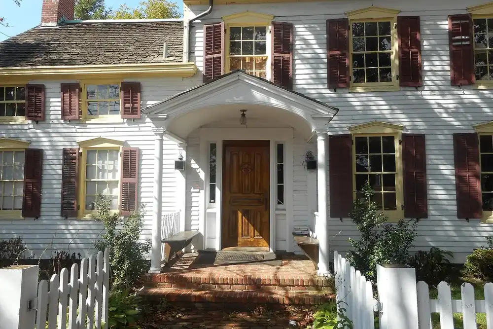 Historic 1826 House with white trim, shutters and a picket fence on West Main Street in Babylon