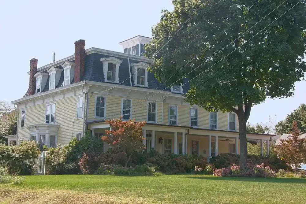 Historic Carll S. Burr Mansion with a mansard roof and flowering shrubs in Commack, New York