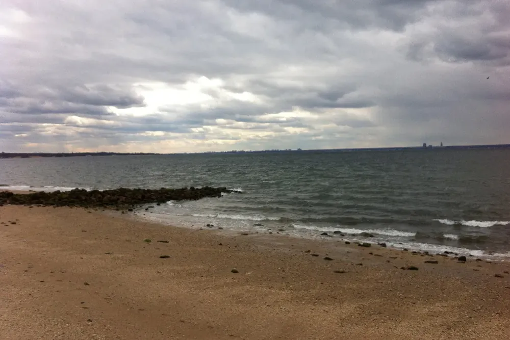 Gravel beach and calm water under a cloudy sky at Welwyn Preserve in Glen Cove, New York