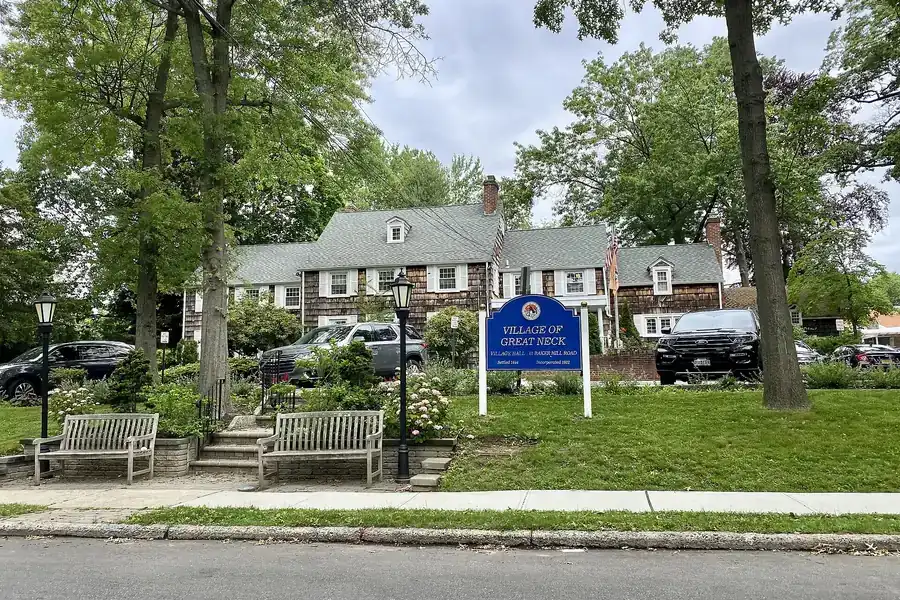 Great Neck Village Hall grounds with benches, trees and a blue village sign in Great Neck, New York