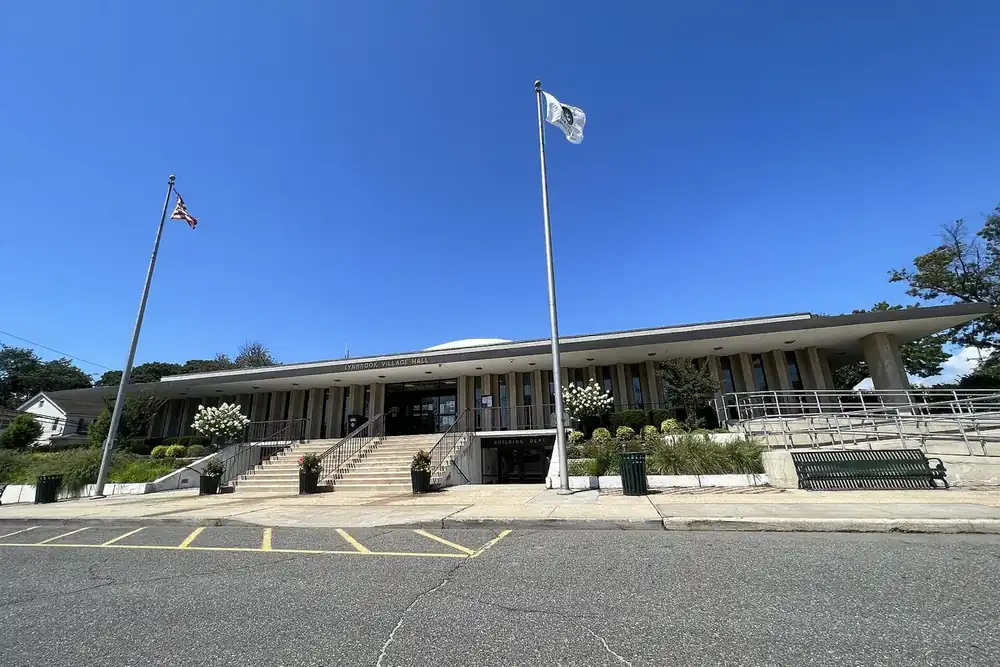 Lynbrook Village Hall, a low modern building with tall flagpoles and a blue sky in Lynbrook