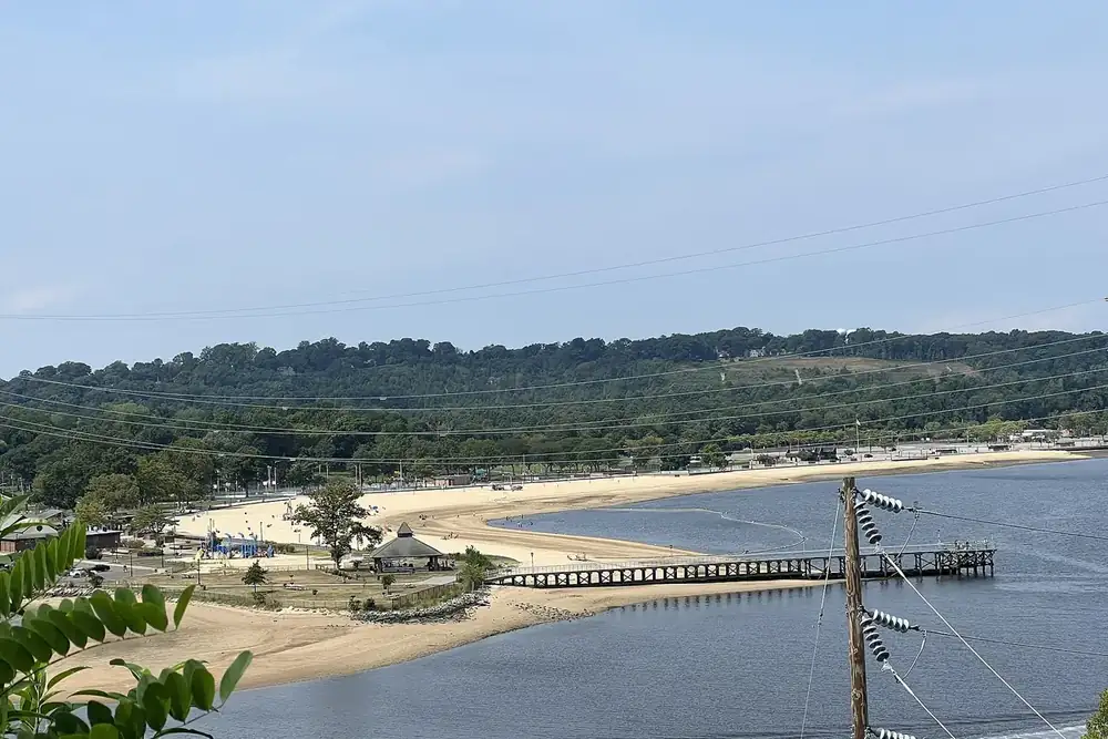 Sandy beach and a long pier along Hempstead Harbor seen from a hillside in Port Washington, New York