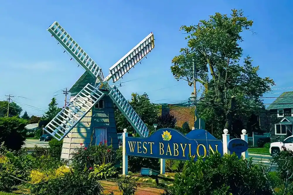 White windmill replica above a West Babylon sign with flowering shrubs in West Babylon, New York
