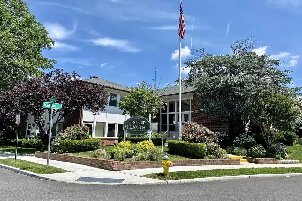 Westbury Village Hall with a flagpole, shrubs and trimmed lawn in Westbury, New York